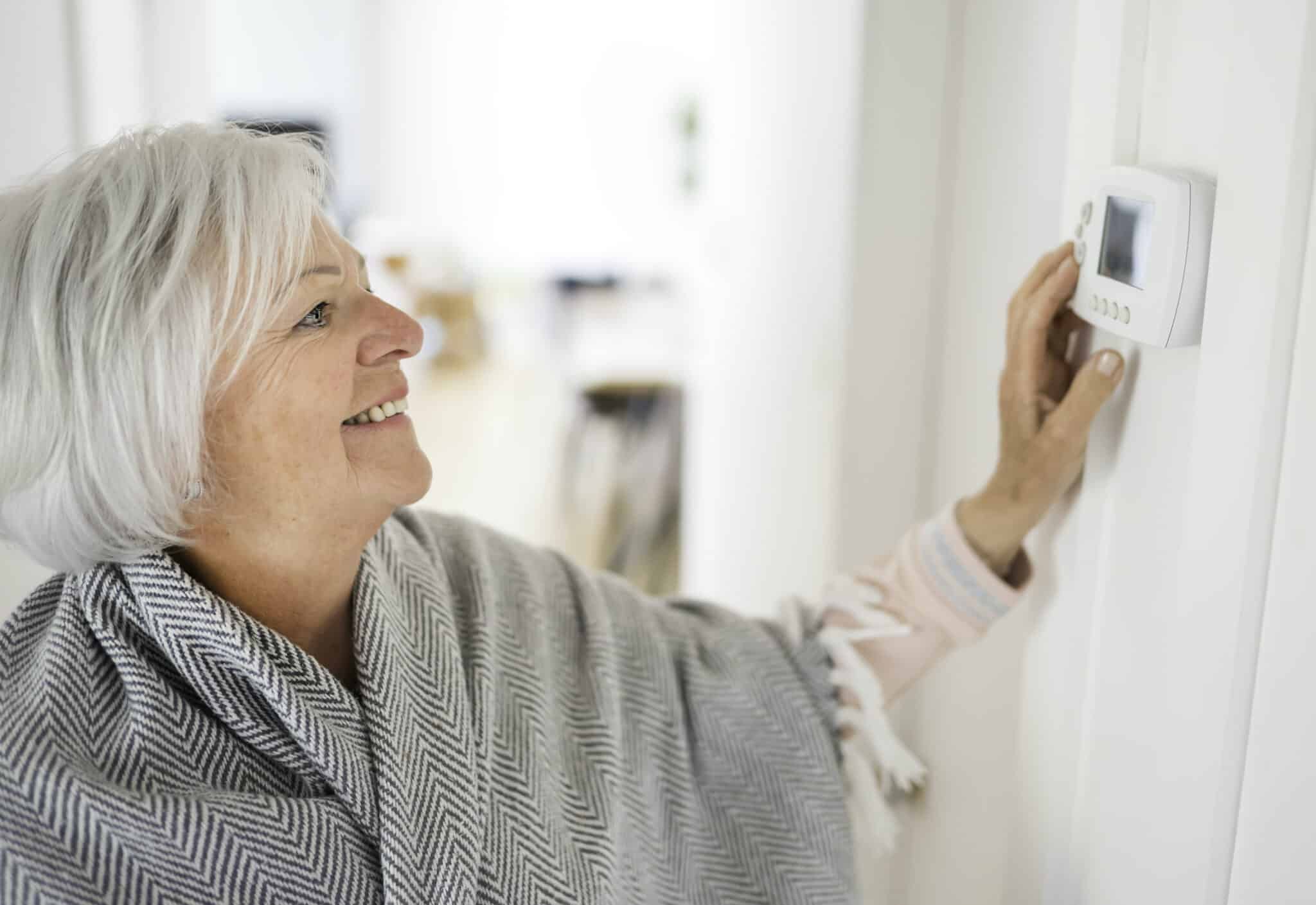 Senior woman adjusting her thermostat at home, Temperature Zoning.